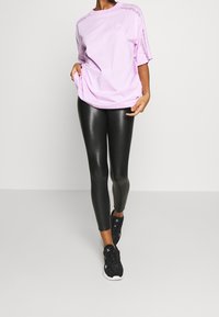 Ljuslila oversized t-shirt med korta ärmar, med en subtil logotyp och spetsdetalj, matchad med tajta svarta leggings och svarta sneakers.