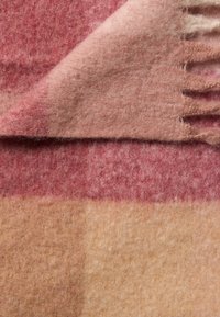 Sciarpa di lana con una miscela di tonalità rosse, rosa e beige, caratterizzata da una texture morbida e lanosa; include bordi frangiati per un tocco di dettaglio.