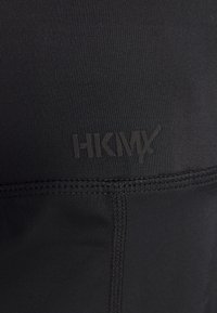 Černé sportovní legíny s texturovanou tkaninou, hladkými švy a jemně embosovaným logem v tmavých tónech podél pasu.