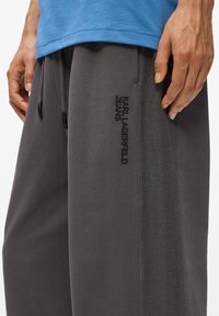 Pelēkie sporta bikses ar teksturētu sānu paneļa, apveltītas ar elastīgu jostasvietu un auklītēm. Izšūts "KARL LAGERFELD JEANS" logo melnā krāsā.