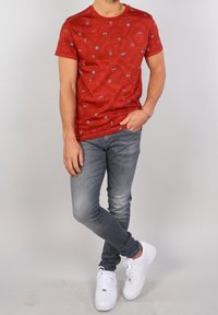 Röd kortärmad t-shirt med ett subtilt mönster av blå symboler, i kombination med grå slim-fit jeans och vita sneakers.