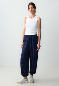 Canotta bianca a coste e pantaloni jogger blu navy larghi con polsini elastici. Modello che indossa sneaker beige con accenti chiari.