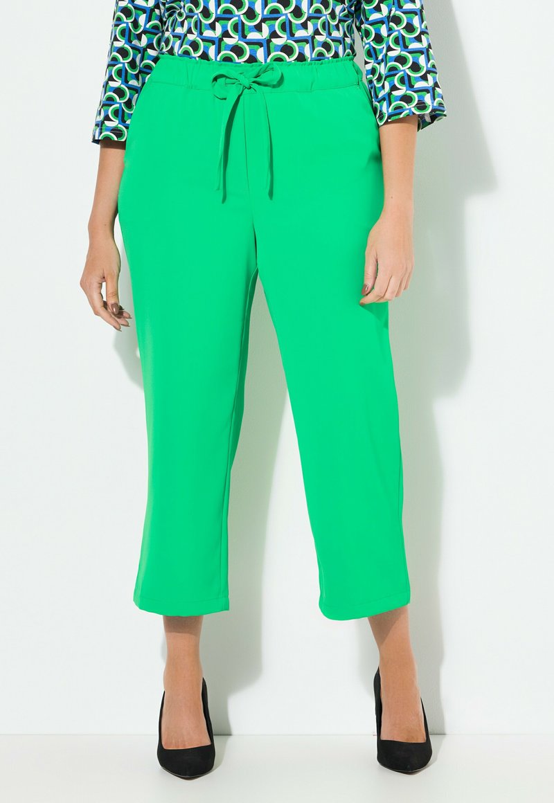 Živé zelené zkrácené kalhoty s tkaničkovým pasem a hladkou texturou, doplněné černými vysokými podpatky.