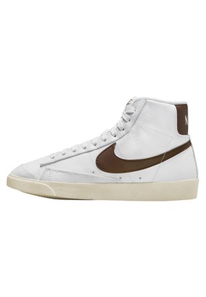 Witte hoge sneaker met bruine Nike-swoosh en hieltab, crèmekleurige zool en witte veters op een effen achtergrond.