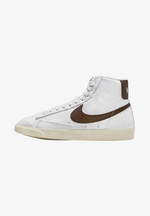 Biały sneaker typu high-top z brązowym znakiem Nike i pętelką na pięcie, kremową podeszwą i białymi sznurowadłami na jednolitym tle.