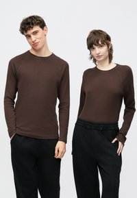 Pruunid pikad varrukad raglaanvarrukatega, mustade pükstega kombineeritud. Kangas tundub sile ning sellel on peened õmblused.