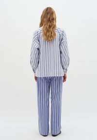 Pigiama a righe blu e bianche. La camicia presenta una vestibilità ampia con maniche lunghe, mentre i pantaloni sono larghi e con righe coordinate.