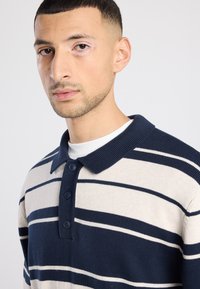 Marineblauw en beige gestreept poloshirt met een kraag, vier knopen en geribbelde manchetten. Gebreide textuur, getailleerd ontwerp.