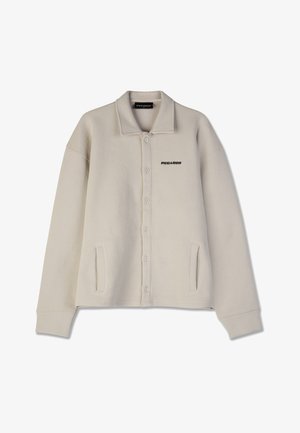 Veste beige à boutons avec un tissu texturé, coupe ample, col, poches latérales et logo "PEGAADOR" sur la poitrine gauche.