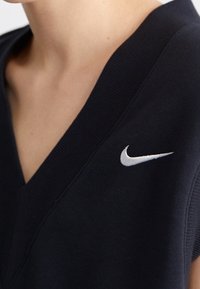 Marinblå Nike ärmlös topp med V-ringning, prydd med en vit broderad logotyp på vänster sida, tillverkad av ett mjukt tyg med len textur.