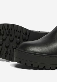 Bottines en cuir noir avec une finition lisse, une semelle en caoutchouc épaisse dotée de motifs de prise hexagonaux et un design à bout arrondi.