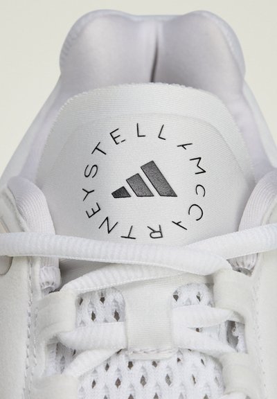 Baltos sportinės bateliai su tinklelio ir sintetiniu viršumi, turintys apvalų logotipą su trimis juodomis juostelėmis ir tekstu "STELLA MCCARTNEY".