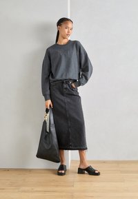 Felpa grigia con logo in rilievo, gonna in denim nera con orlo sfilacciato, sandali neri a scivolo e una grande borsa a tracolla nera con accentuazione a catena.