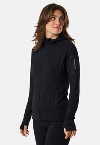 Svart zip-up jacka gjord av stretchigt tyg. Har en huva, två zipparade sidofickor och en ärmficka med logotyp. Långa ärmar med tumhål.