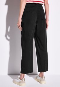 Svarta vida byxor med hög midja, slät struktur, två bakfickor och en ren fåll. Bärs med vita sneakers.