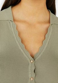 Olijfgroen geribbeld vest met een gegolfde kraag, voorzien van decoratieve knopen, met een textuurstof en een V-hals ontwerp.