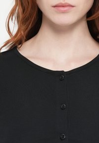 Top negru cu rebrare, având un decolteu în formă de u și șase nasturi frontali, cu o textură netedă și o siluetă ajustată.