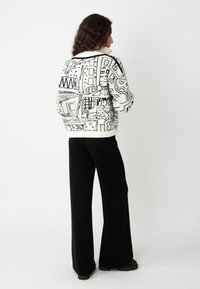 Gebreide oversized trui in het wit met zwarte grafische patronen, met verschillende geometrische vormen. Gecombineerd met zwarte wijde broek.
