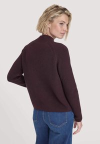 Maglione a collo alto di colore bordeaux in maglia, con maniche raglan e un motivo testurizzato. Indossato sopra dei jeans blu, presenta una vestibilità rilassata.