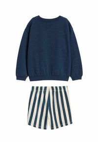 Tummansininen collegepaita pyöreällä kaula-aukolla ja pitkillä hihoilla, yhdistettynä vaaleanbeigeihin ja tummansinisiin raidallisiin shortseihin. Molemmat ovat rentoa istuvuutta.