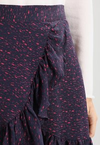 Jupe bleu marine avec un motif à pois roses, présentant un détail froncé sur le côté et un ourlet évasé. Fabriquée en tissu doux et texturé.