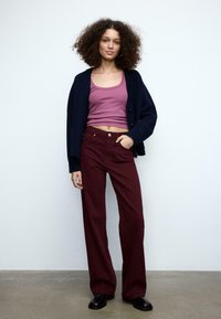 Marineblå cardigan over en pink ærmeløs top og bordeaux bukser med brede ben. Ensfarvede, glat tekstur og minimale detaljer i outfittet.