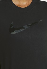 Camiseta de algodón negra con un logotipo de Nike en camuflaje negro brillante en el frente. Diseño de cuello redondo, textura suave y corte relajado.