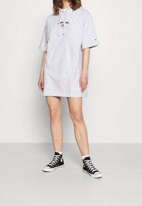 Šedé šaty s krátkým rukávem a kapucí, s přední kapsou, zdobené grafickým logem a volným střihem. V kombinaci s černými vysokoškolskými teniskami.