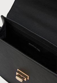 Μαύρη τσάντα χειρός με απαλό συνθετικό εξωτερικό, χρυσό μεταλλικό κούμπωμα και εσωτερική τσέπη με φερμουάρ. Το εσωτερικό διαθέτει μαύρη υφασμάτινη επένδυση.