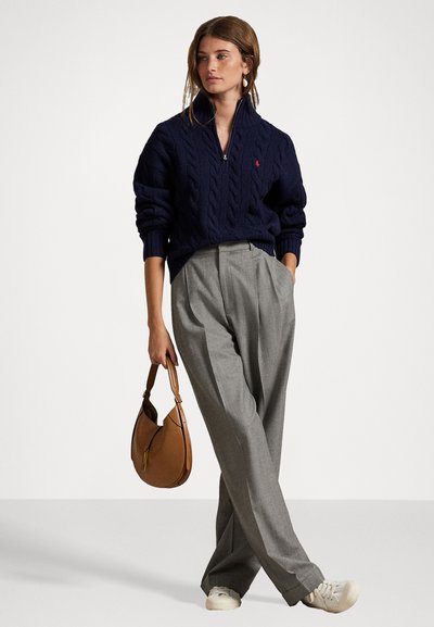 Navy knitted cable sweater, gray tailored pleated trousers, beige handbag, and white sneakers create a classic, relaxed look.
