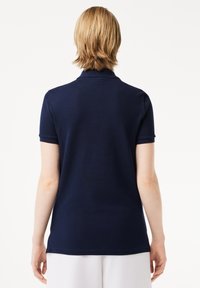 Granatowa koszulka polo z krótkim rękawem, klasycznym kołnierzykiem i gładką fakturą. Widok z tyłu ukazuje czysty krój i minimalne detale przyszycia.