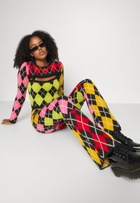 Conjunto de malha em duas peças com um padrão argyle multicolorido em rosa, verde, vermelho, amarelo e preto. Botas grossas pretas completam o visual.
