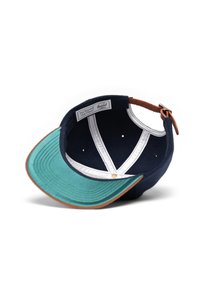 Gorra con cuerpo azul marino y visera de color teal contrastante, además de detalles de cuero marrón claro. El interior presenta un forro blanco y orificios de ventilación.