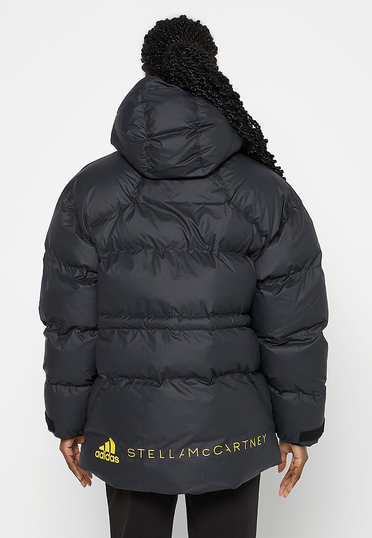 Schwarze Steppjacke mit Kapuze, mit gesteppten Abschnitten, elastischen Bündchen und gelber Logo-Schrift auf der Rückseite, aus synthetischem Material.