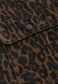 Tissu marron avec motif léopard noir et un bouton pression noir sur une poche à rabat cousue.