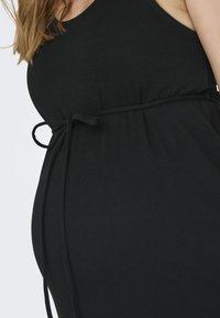 Robe noire sans manches en tissu doux avec une taille froncée et un détail de nœud, conçue pour le confort et une silhouette fluide.