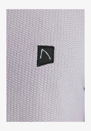 Tekstuirana vijolična tkanina z mrežastim vzorcem in črno pravokotno oznako z belo abstraktno obliko.