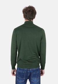 Maglione verde a maglia con collo alto, forma aderente e polsini a costine, abbinato a jeans in denim azzurro.