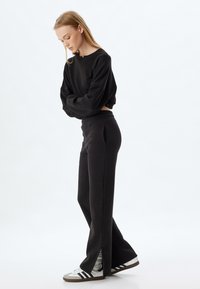 Zwarte, oversized sweatshirt met een ronde hals en lange mouwen. Zwarte, taps toelopende joggers met zijzakken en inkepingen aan de onderrand.