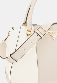 Witte synthetische handtas met textuurafwerking, voorzien van gouden hardware, een verstelbare schouderriem en een driehoekig logo-accent aan de voorkant.