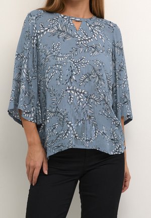 Top azzurro con motivo floreale, scollatura a chiave e maniche larghe. Realizzato in tessuto texturizzato, abbinato a jeans neri.