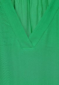 Blouse verte à col en V, fabriquée dans un tissu léger avec une surface texturée et un détail froncé au niveau de l'encolure. Couleur unie avec des lignes épurées.