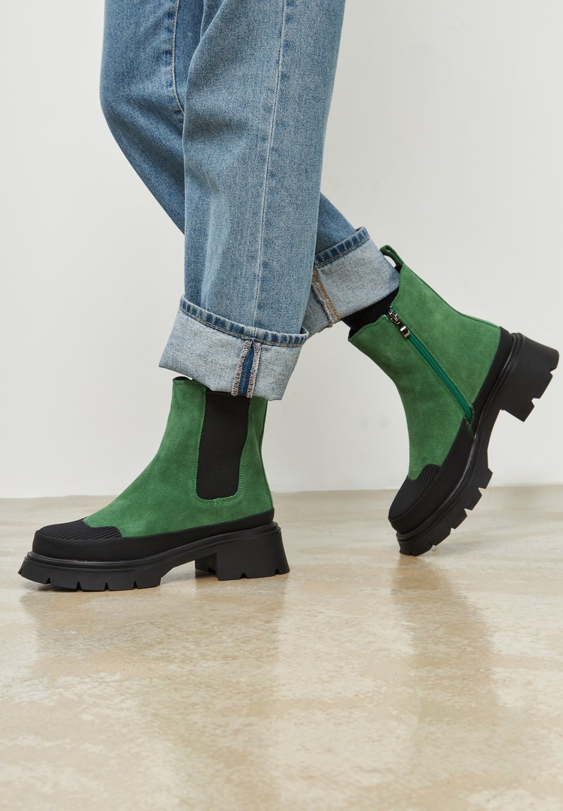 Groene suede enkellaarsjes met zwarte accenten, stevige rubberen zool, een zijrits en elastische inzetten. Gedragen met opgerolde lichtblauwe spijkerbroeken.