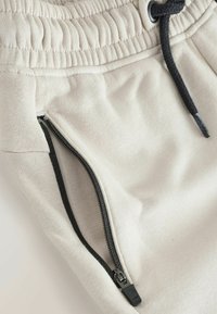 Beige jogger pants made from soft fabric, featuring an elastic waistband and black zipper pocket detailing on the side.