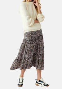 Maglione color crema con texture e maniche voluminose, abbinato a una gonna fluida con stampa leopardata e orlo svasato, completato da sneakers sportive.