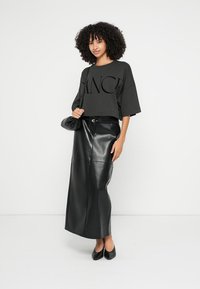 T-shirt preta cropped com grande estampa "DANCE", combinada com saia maxi de cintura alta em pele sintética preta; modelo segurando uma bolsa preta.