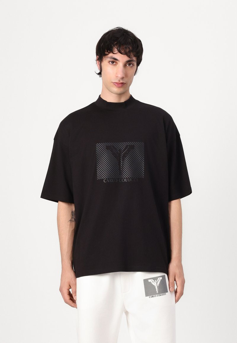 Zwarte T-shirt met een hoge hals, oversized pasvorm, voorzien van een vierkante graphic met strepen en de tekst "CARLO COLUCCI" in het midden.