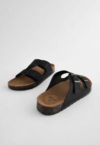 Sandali neri con due cinturini regolabili, dotati di una suola con texture in sughero e un plantare beige, progettati in uno stile facile da indossare.