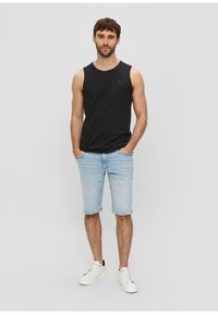 Černý bezrukávový top spojený s světle modrými denimovými kraťasy. Bílé sneakers doplňují neformální outfit a ukazují uvolněný střih.