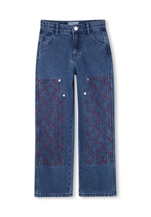 Jean en denim bleu avec de grandes pièces aux genoux avant comportant des motifs de pièces de puzzle rouges cousues et des détails de boutons argentés.